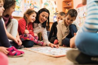 Happy female teacher teaching group of small kids in a preschool.